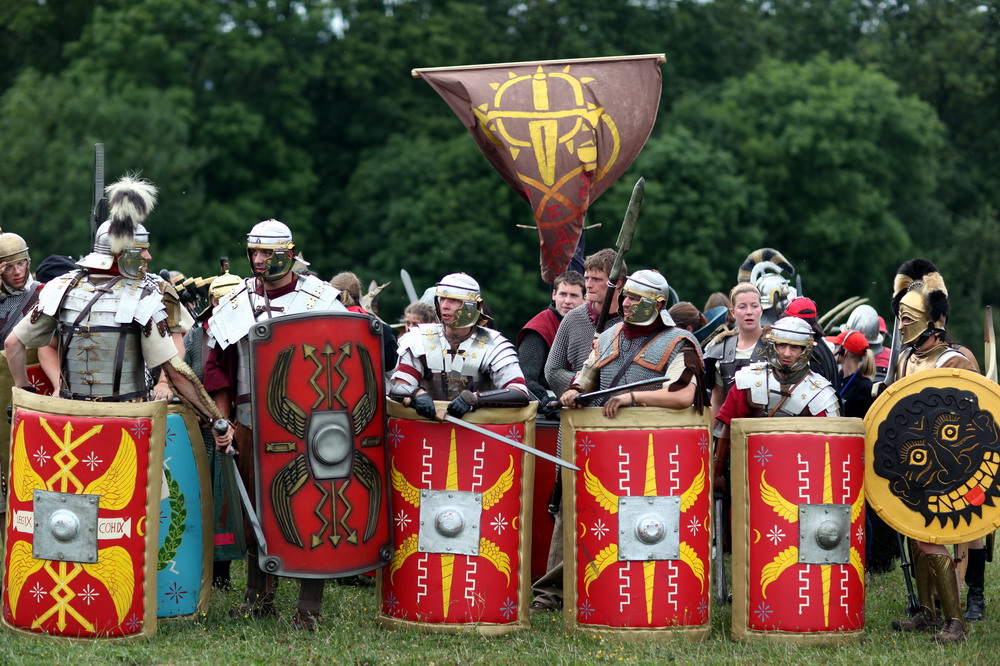 a group of people wearing armor, holding shields and swords, and raising a red flag on the field